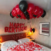 A bed decorated with red petals and a string of red balloons spelling out HAPPY BIRTHDAY