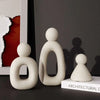 Three smooth, beige resin figures in different sizes standing on a white box.