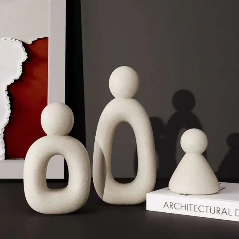 Three smooth, beige resin figures in different sizes standing on a white box.
