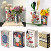 A ceramic book-shaped vase with a vintage finish decorated with floral patterns and leaves.