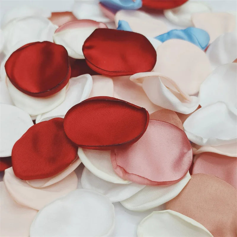 A close-up of various silk rose petals in shades of red, pink, and white scattered on a surface.
