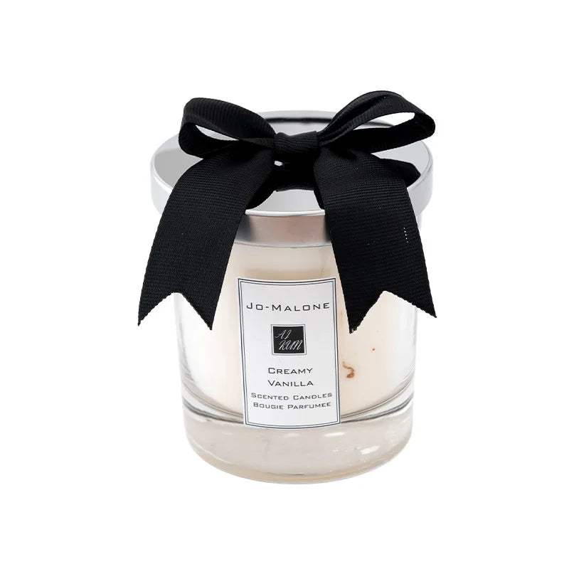 A glass candle cup with a black ribbon tied around the lid, labeled Jo Malone Creamy Vanilla scented candles.