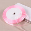 Pink satin ribbon spool with a loose strand unwound on a white background.