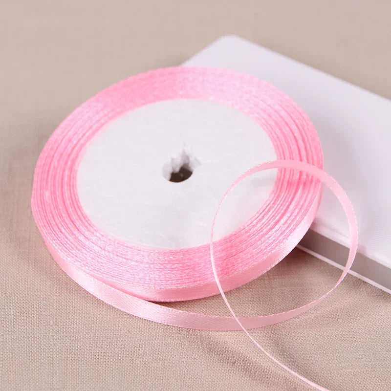 Pink satin ribbon spool with a loose strand unwound on a white background.