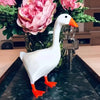 A white ceramic goose figurine with an orange beak stands next to a silver key holder on a dark surface.