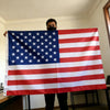 A person holds up a double-sided American flag with brass grommets indoors.