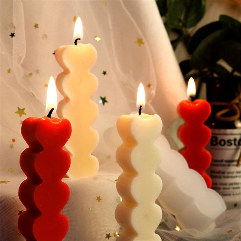 A set of two heart-shaped silicone candle molds in red and white are displayed on a white cloth.