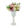 A white ceramic pedestal vase filled with a bouquet of pink, purple, and cream roses and greenery.