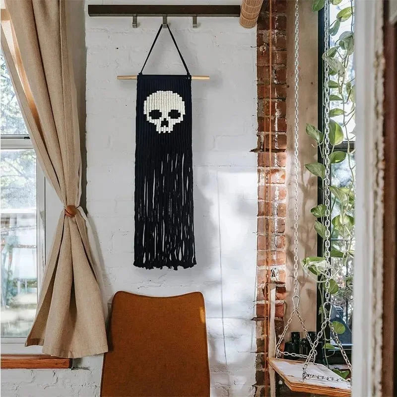 Tapis mural en macramé noir avec un crâne blanc accroché sur un mur de briques blanches.