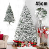 A large flocked artificial Christmas tree decorated with white snow, placed in a living room setting.