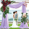 Arco de boda decorado con tela morada, arreglos florales y follaje verde de ruscus italiano.