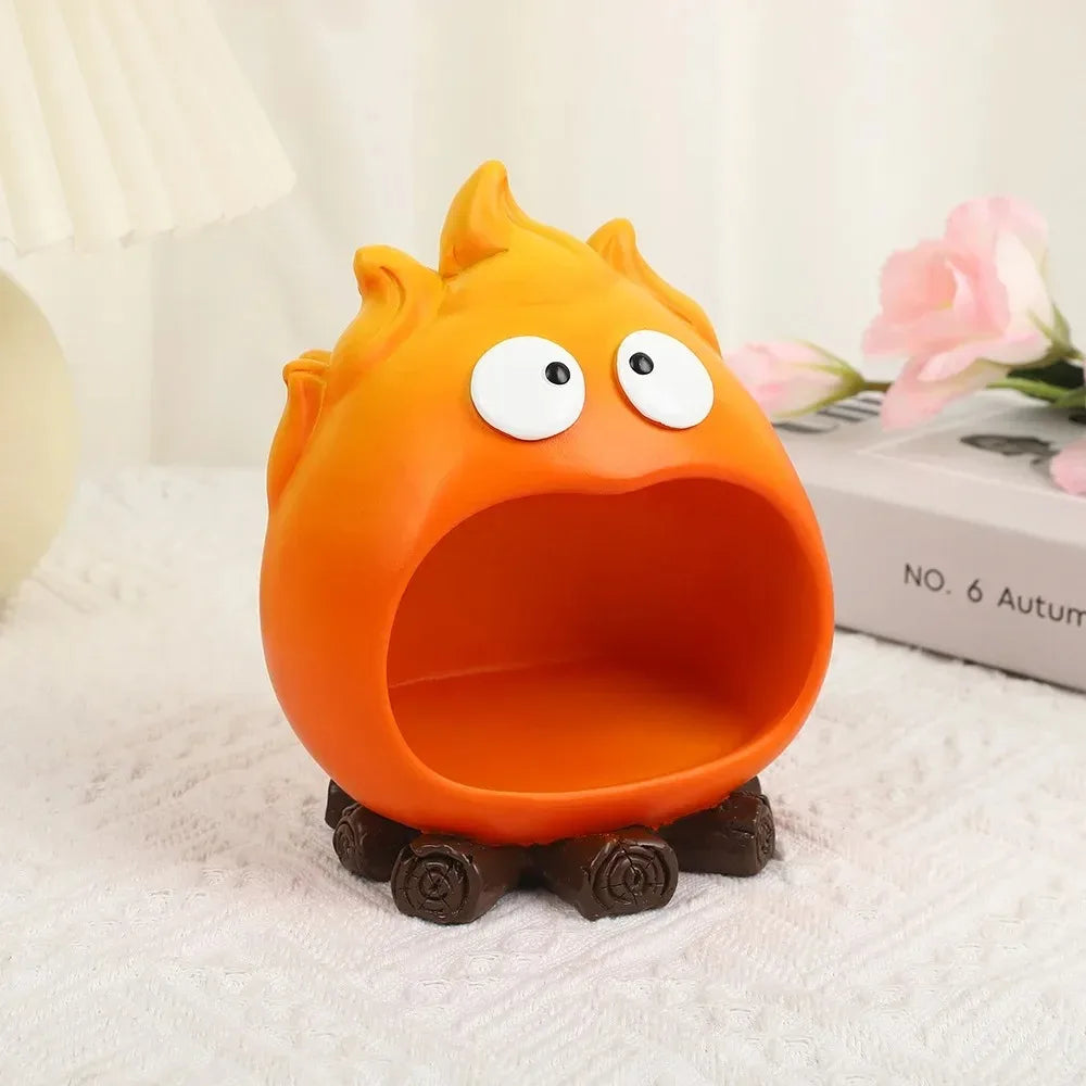 An orange resin fire spirit figurine with wide eyes sits on a white towel next to a box.