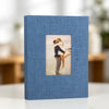 A blue linen photo album with a square display window showing a couple embracing.