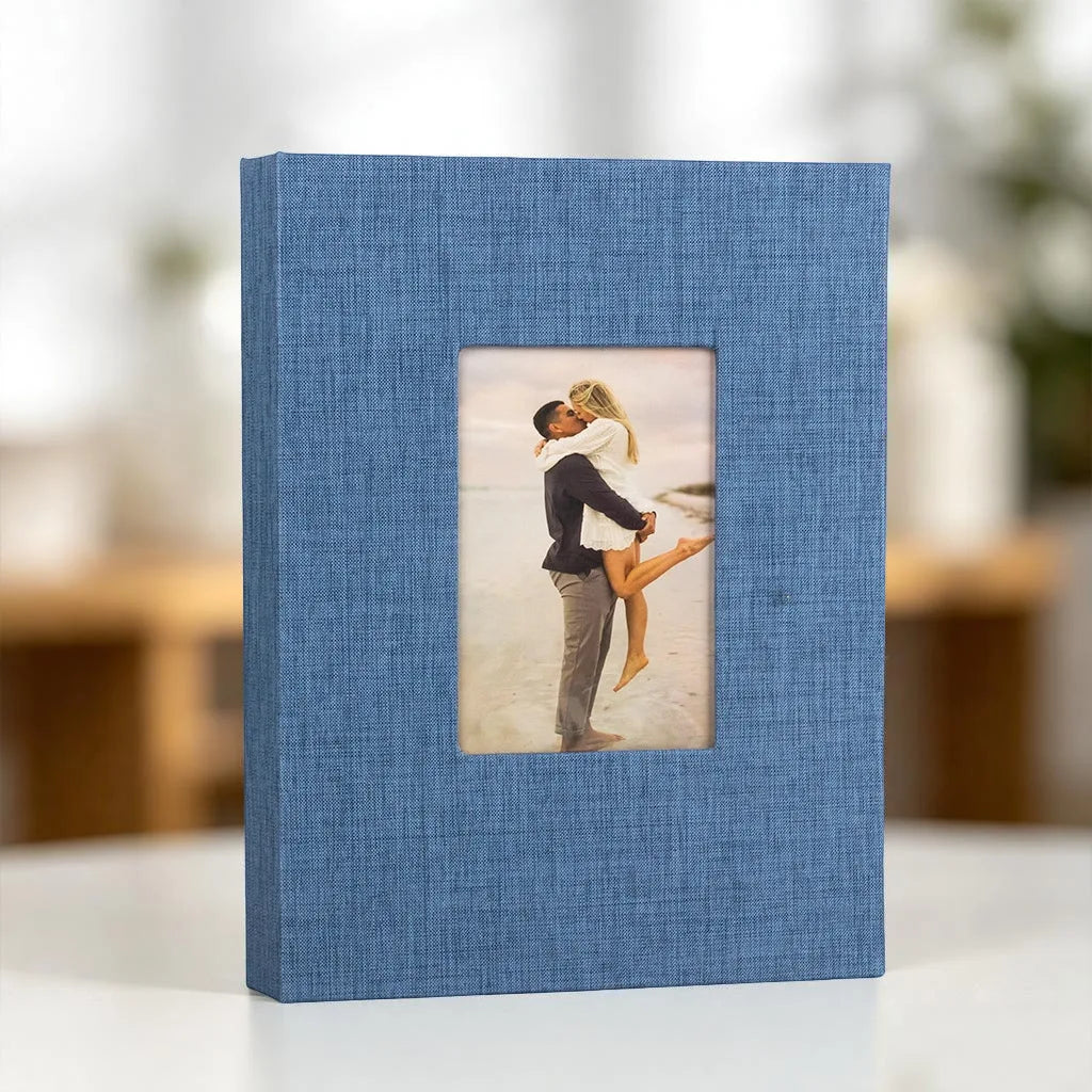 A blue linen photo album with a square display window showing a couple embracing.