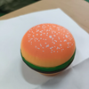 An orange squishy food-shaped stress ball resembling a burger with white dots, placed on a white surface.