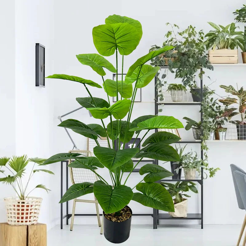 A large, lush artificial green tree with broad leaves displayed in a black pot on a shelving unit.
