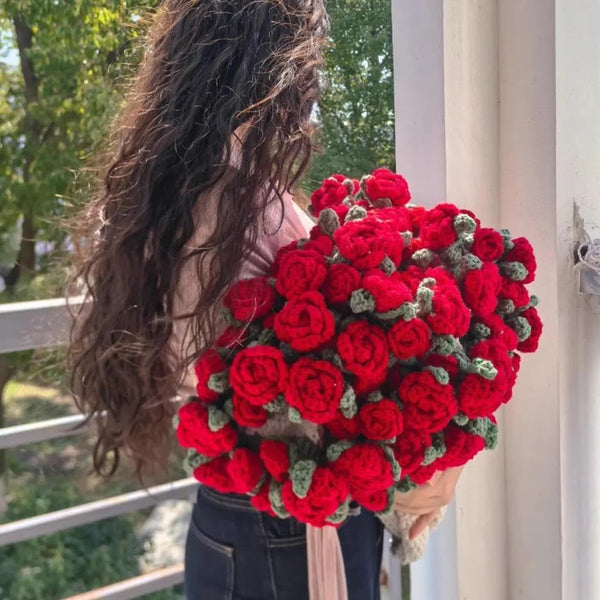 Un bouquet vibrant de roses rouges enveloppé dans un tissu doux, tenu par une personne près d'une fenêtre.