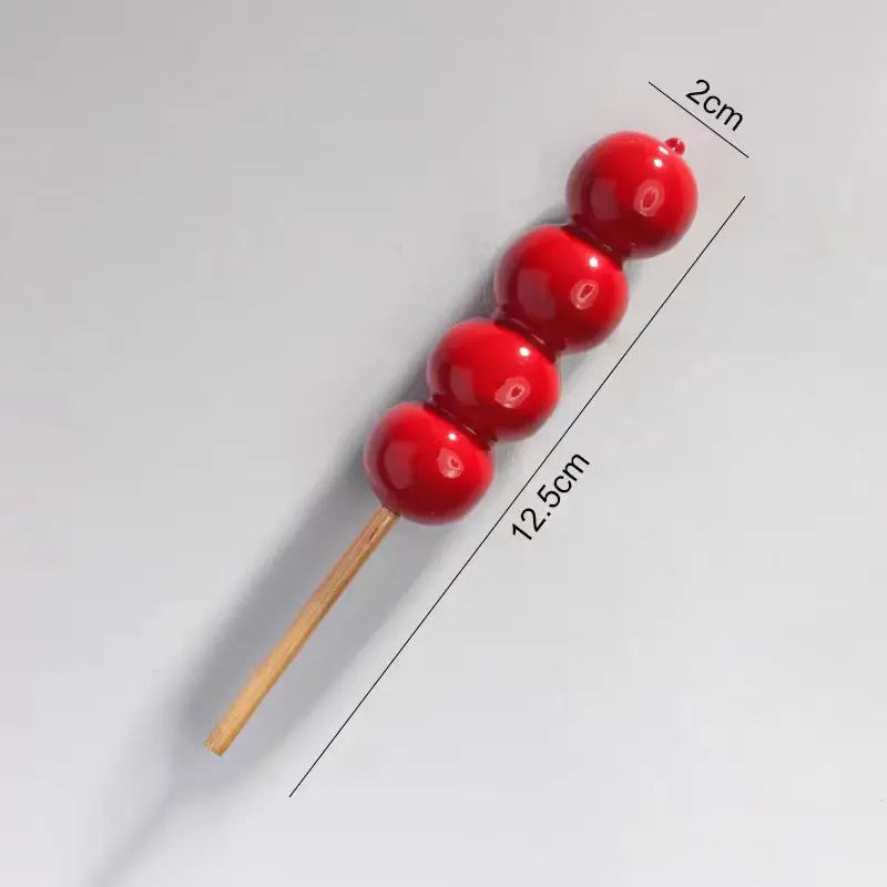 A set of three glossy red spherical fridge magnets resembling fruit, mounted on a wooden stick.