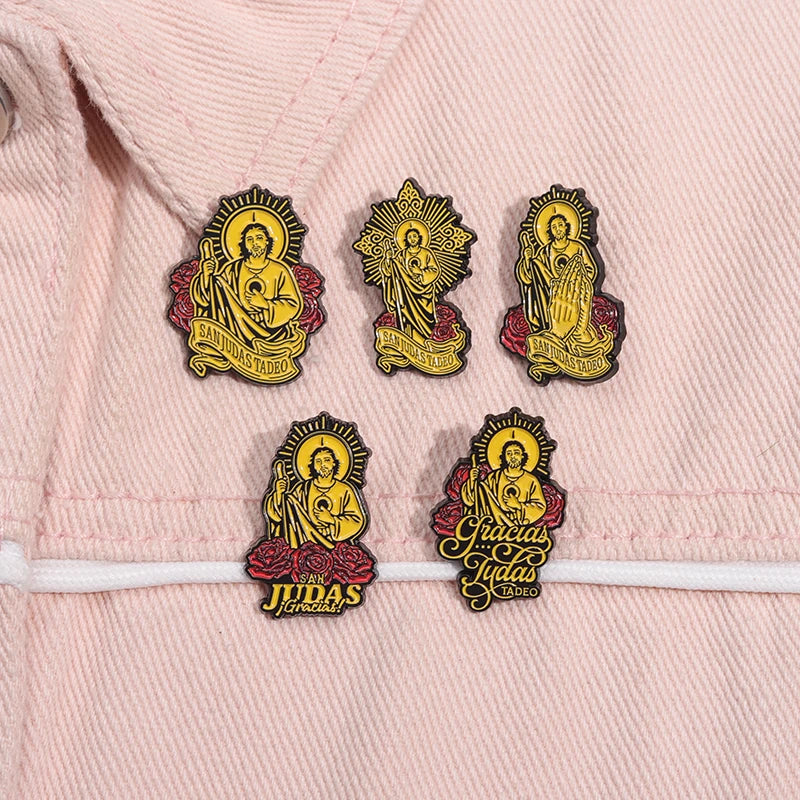 Gold enamel pins featuring religious figures of Saint Judas Tadeo on a pink fabric background