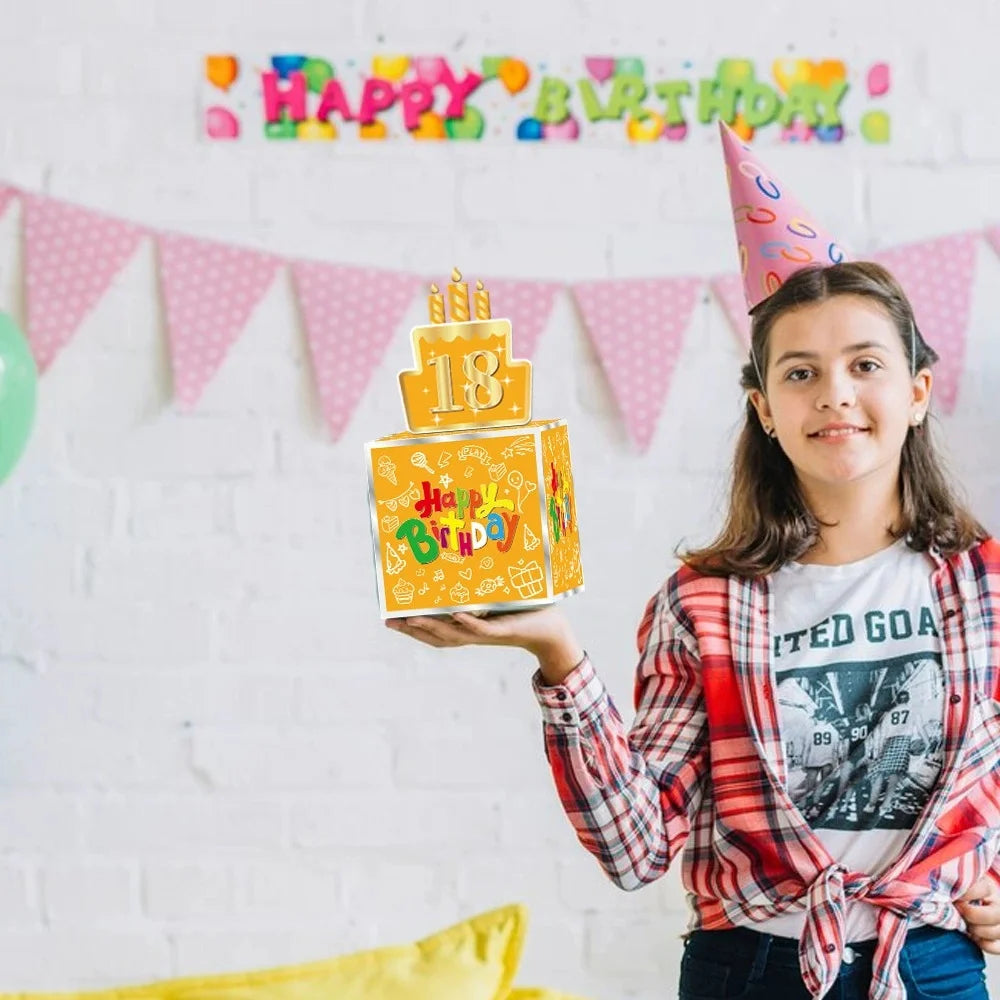 A girl holds up a yellow birthday gift box decorated with stickers and a crown against a white brick wall backdrop.