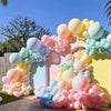 A colorful balloon garland arch featuring pastel colors like pink, blue, and yellow, set outdoors.