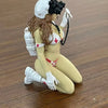 A female rifleman desktop figurine with long brown hair, wearing a white uniform and gloves, sitting on a wooden surface.
