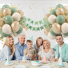 A festive birthday celebration setup featuring sage green and gold confetti balloons, cake, and drinks.