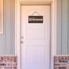 A white door with a wooden welcome sign hanging above it, set in a light-colored frame.
