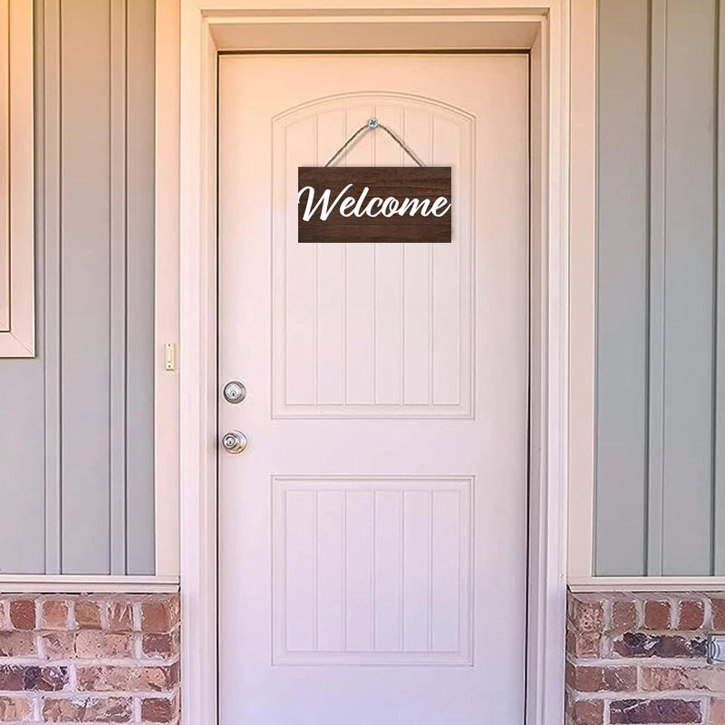 A white door with a wooden welcome sign hanging above it, set in a light-colored frame.