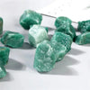 A collection of raw green aventurine crystal stones scattered on a white surface.