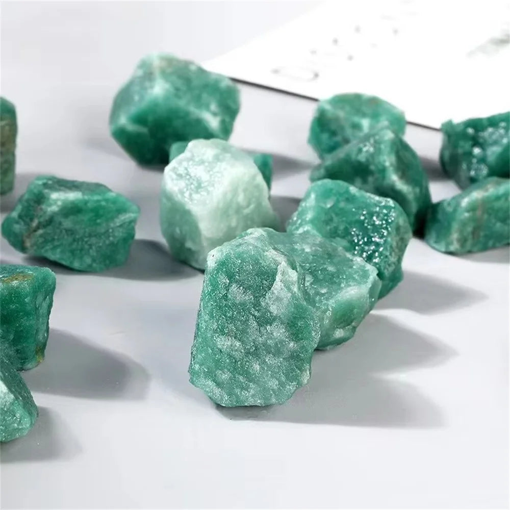 A collection of raw green aventurine crystal stones scattered on a white surface.