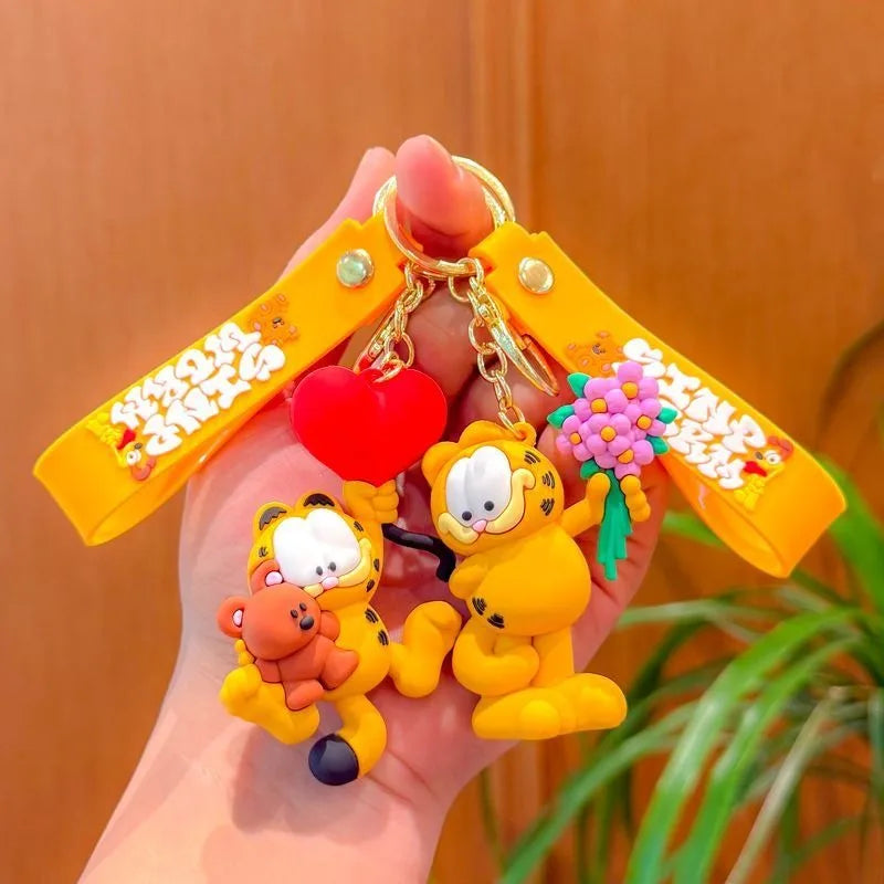 A hand holds a yellow keychain pendant featuring Garfield cartoon characters, including a bear and a cat.