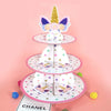 A three-tier rainbow cupcake stand featuring pink and purple floral accents and a gold unicorn topper.