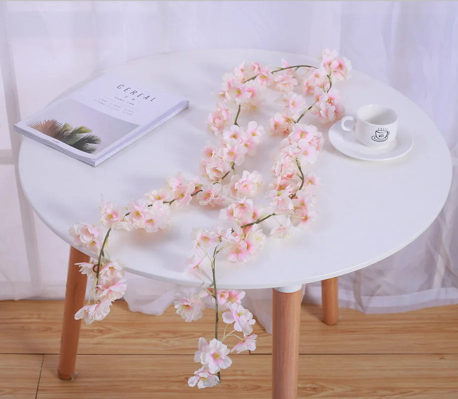 A white table features a pink sakura flower garland and a book, set against a light background.