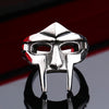 A silver stainless steel mask ring with a pointed design, reflecting on a dark surface.