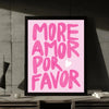 A framed print featuring the text MORE AMOR POR FAVOR in bright pink script on a light pink background.