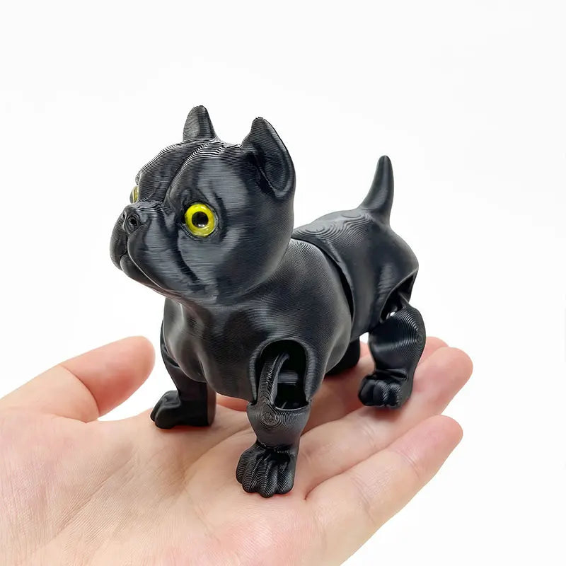 A black 3D printed articulated bulldog figurine is held in a person's hand.