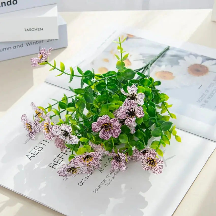 A bouquet of silk eucalyptus and violet artificial flowers displayed on a white background.