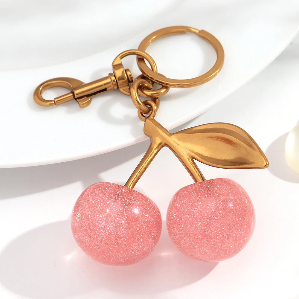 A gold-toned resin pink cherry pendant keychain attached to a split ring.