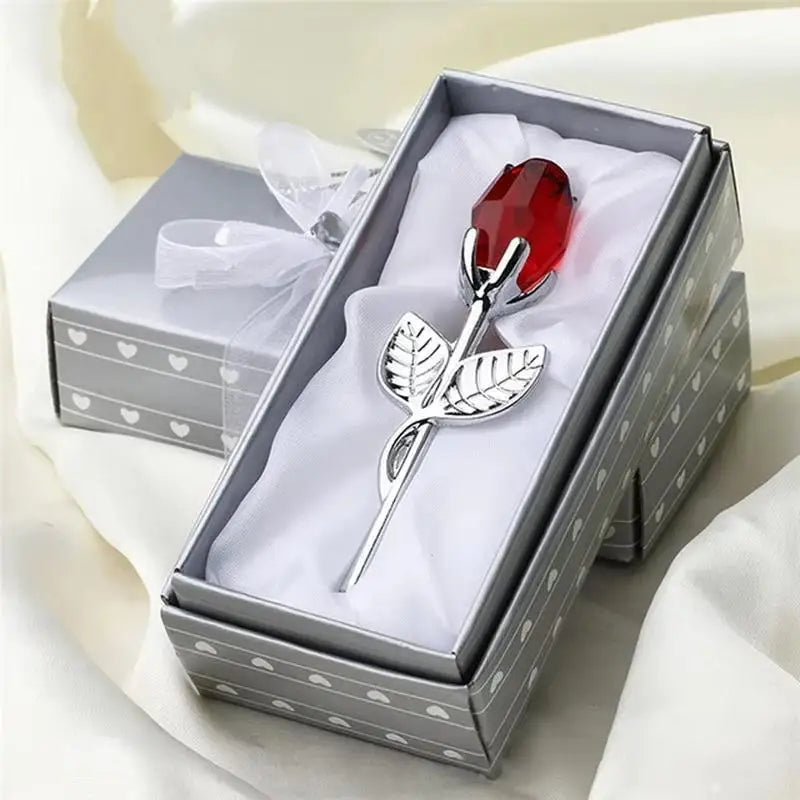 A silver crystal rose artificial flower is displayed in a square box with white lining and a gray patterned lid.