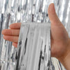 Une main tient une bande verticale de rideaux à franges en feuille d'argent arc-en-ciel.