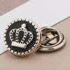 A round black and gold crown brooch button with a silver finding on a light background.