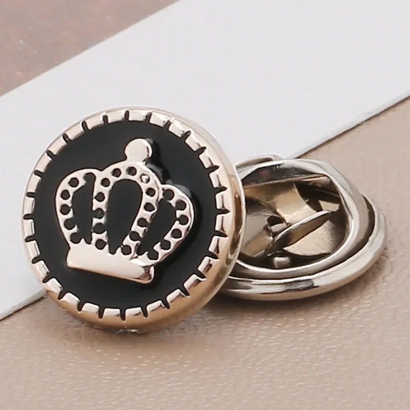 A round black and gold crown brooch button with a silver finding on a light background.