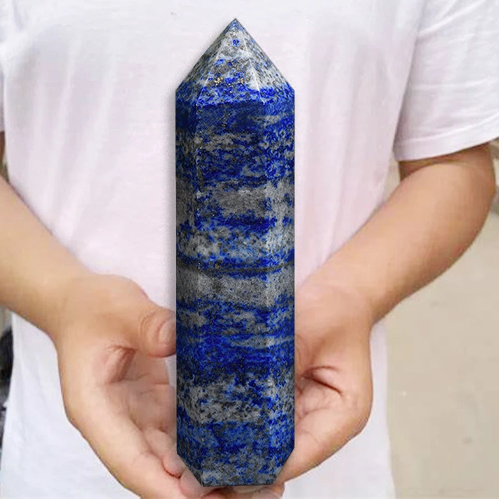 A hand holds a polished blue and gray Lapis Lazuli crystal tower for meditation and home decor.