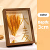 A wooden shadow box frame containing dried wheat stalks and gold geometric shapes.