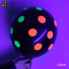 A hand holds a black latex balloon with glowing neon green and orange dots against a purple background.