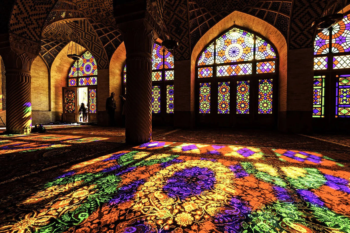 Interior view of a mosque with intricate stained glass windows and colorful floor art.