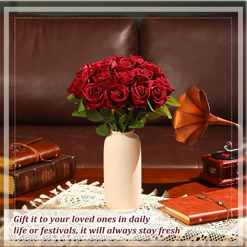 A bouquet of deep red artificial silk roses in a beige vase set on a wooden surface.