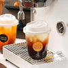 A clear disposable coffee cup with a white lid is placed on a metal rack inside a white appliance.