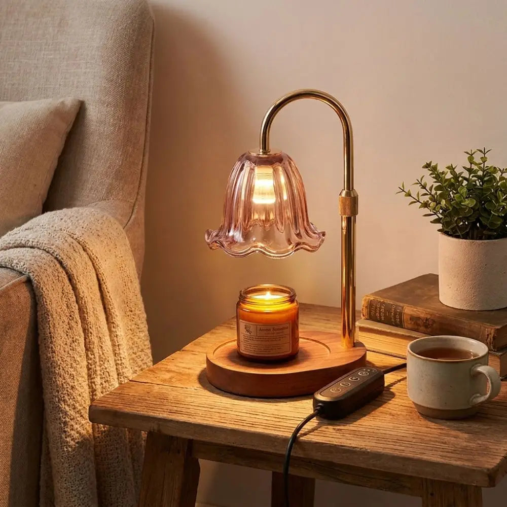 A brass adjustable height aromatherapy candle warmer lamp with a glass shade and a wooden base sits on a light wood table.